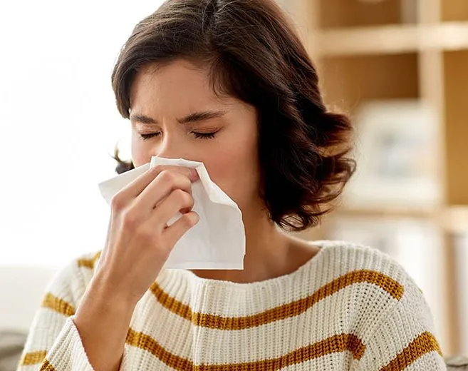 sick woman blowing nose in paper tissue