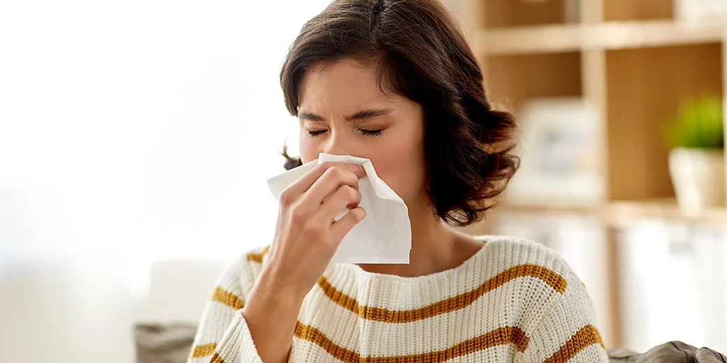 sick woman blowing nose in paper tissue