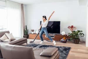 Young happy woman listening and dancing to music while cleaning the living room floor with a vacuum cleaner